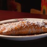 A beautifully plated cannoli filled with rich chocolate cream and topped with crushed pistachios.